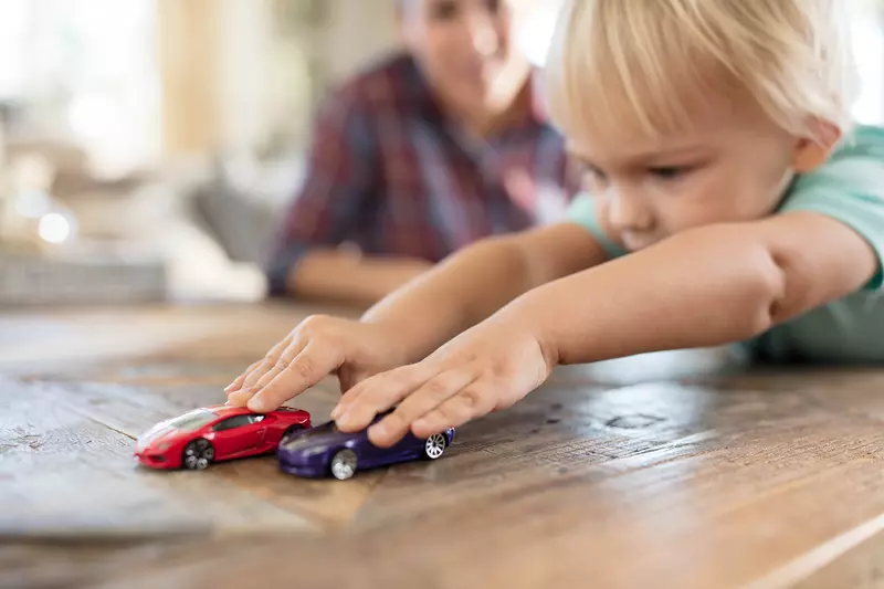 Little Boy Playing with Cars with Father in Background 