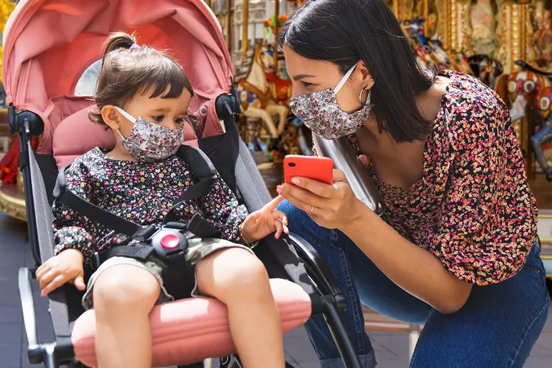 A mom and her young daughter wearing masks at a theme park.