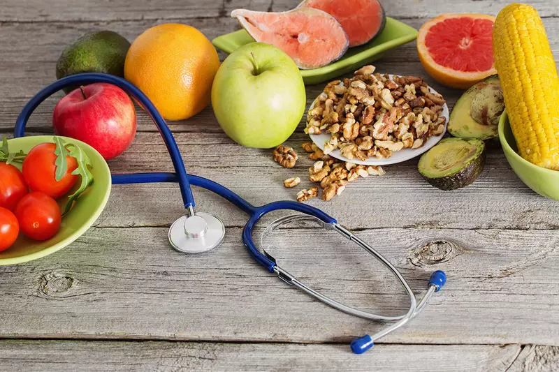 A spread of fruits and vegetables around a stethoscope on a wooden table