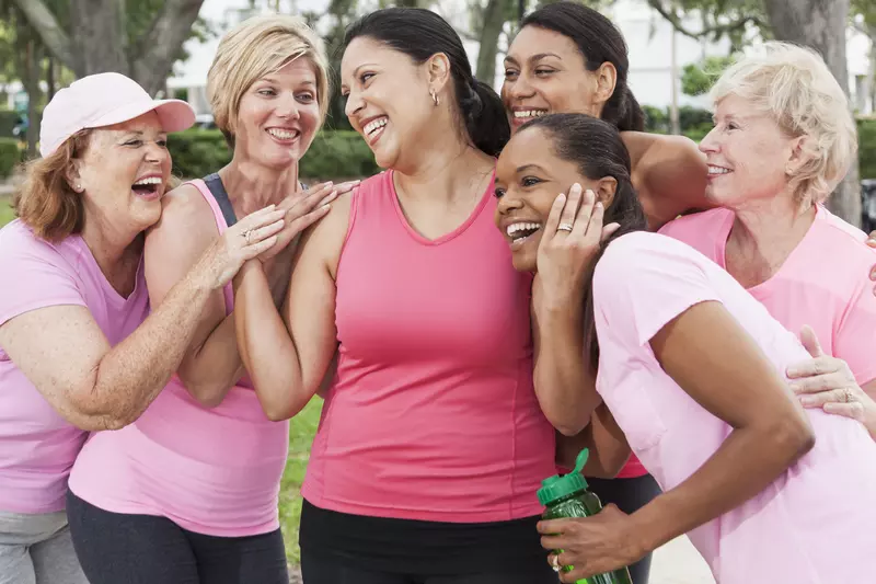 A group of friends, all wearing pink and hugging a woman in the venter, to support a breast cancer survivor.