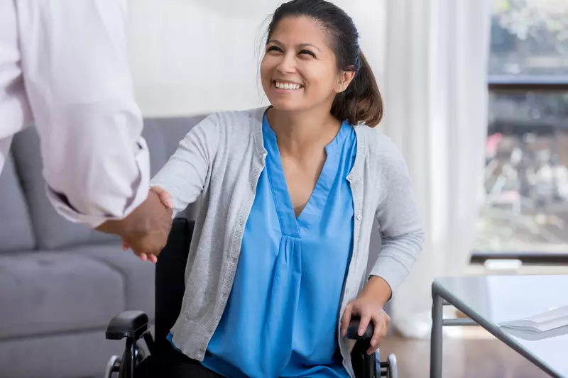 A woman in a wheelchair is shaking hands with a doctor.