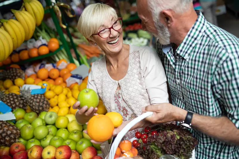 A senior couples shopping for produce with a basket.