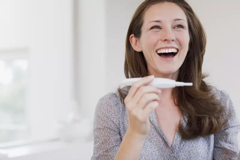 Happy woman laughs at the positive pregnancy test
