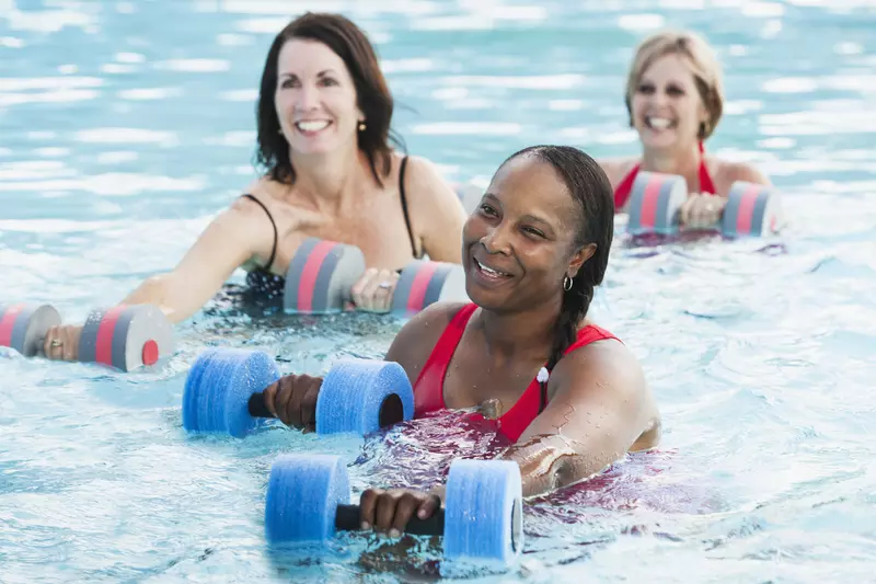 Three women building knee strength in a water aerobics class.