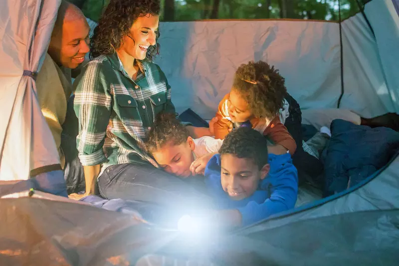 A family of five is snuggled together in a tent with a flashlight on.