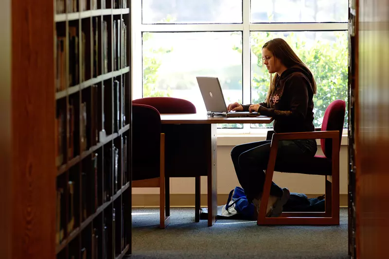 A girl sitting at a table in the library on her laptop.