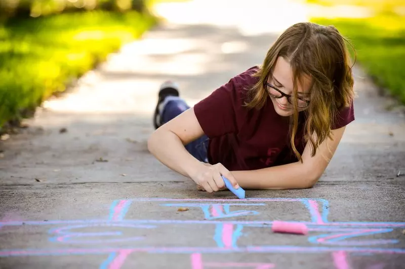 Girl chalks hopscotch game on sidewalk