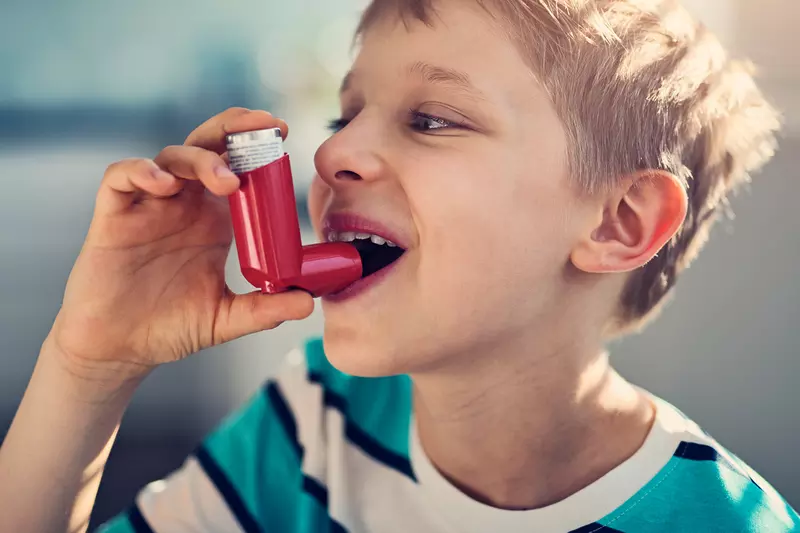 Young boy smiling about to take a puff from an inhaler.