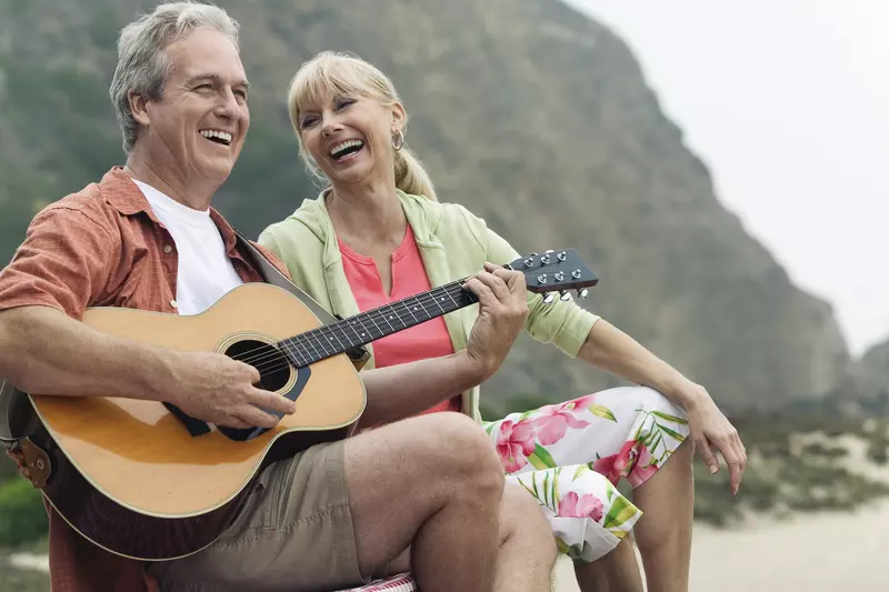 A couple playing guitar on the beach.