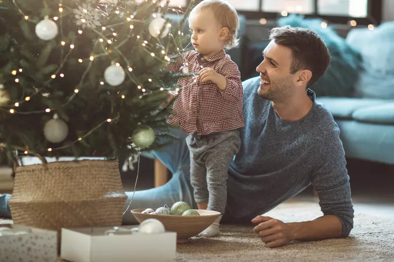 A father and his toddler trim a Christmas tree.