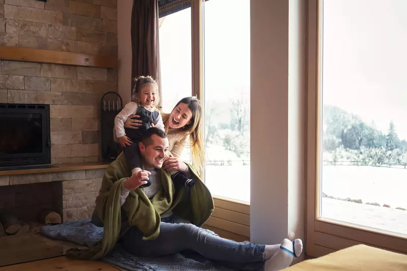 A young family plays together indoors by a window at home