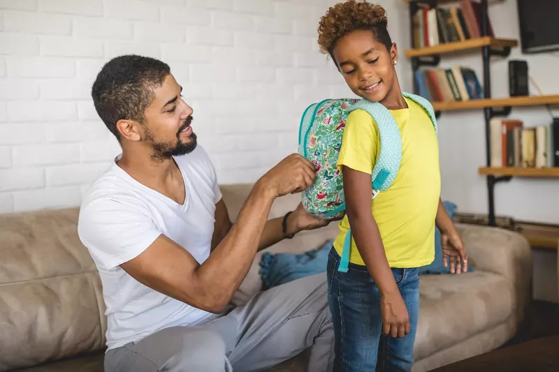 A father adjusts his child's backpack.