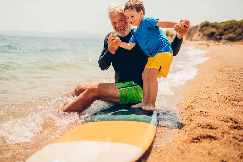 A grandfather teaches his grandson to surf.