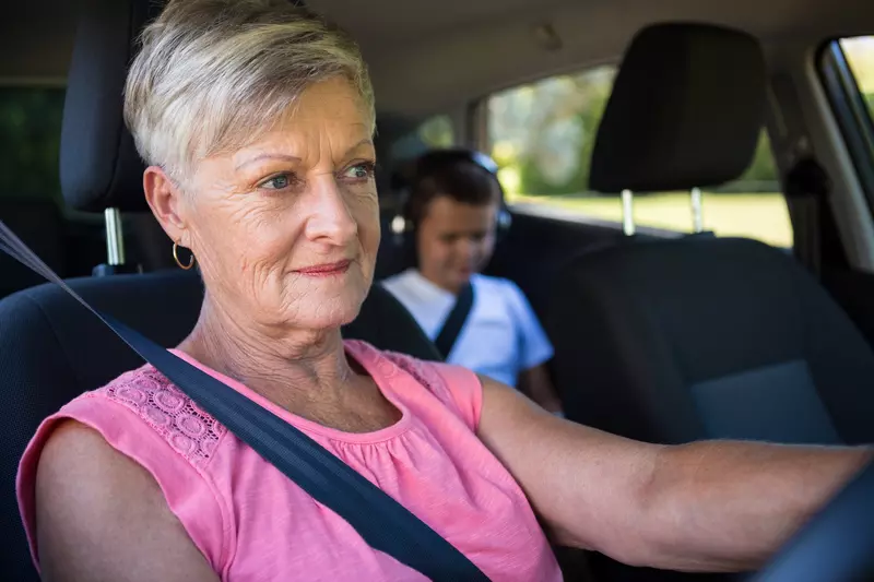 A grandmother driving with her grandson in the back seat.