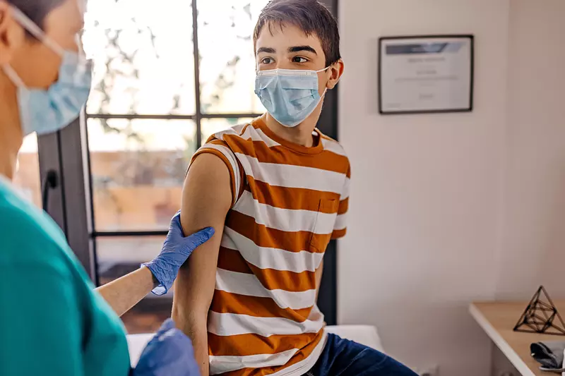 A teenager getting a vaccine shot by a nurse