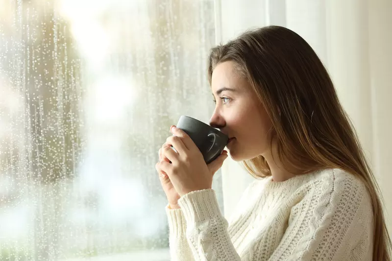 A woman drinking indoors while looking through the window