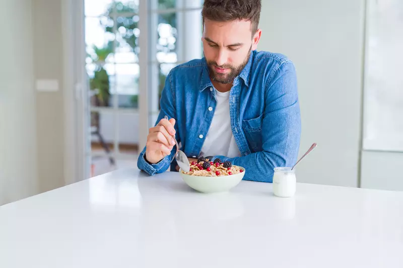 A gentleman eating a bowl of cereal with berries and a cup of yogurt