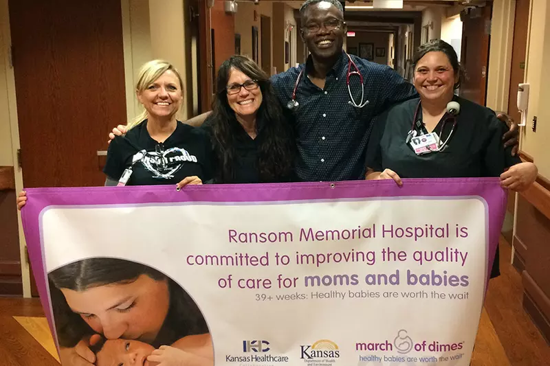 Physician and nurses holding a banner of the work they do for mothers and babies.