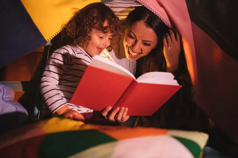 A mom and daughter read together by flashlight.