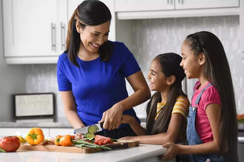 A mom chopping vegetables with her daughters in the kitchen.