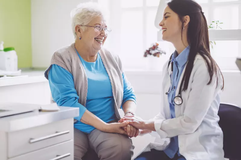An older woman laughs with her doctor during a visit.