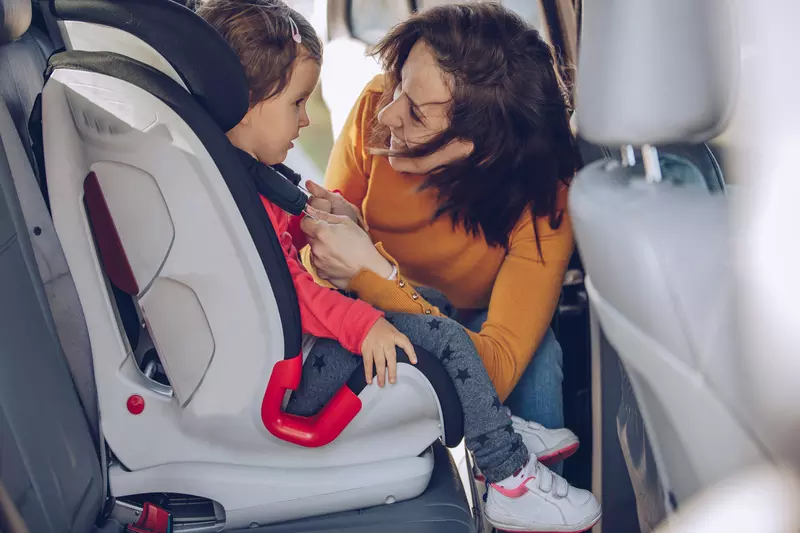 A mom buckles her toddler into her carseat.