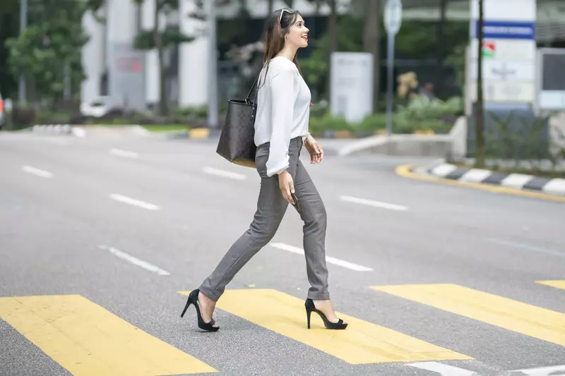 A woman crosses the street wearing high heels.
