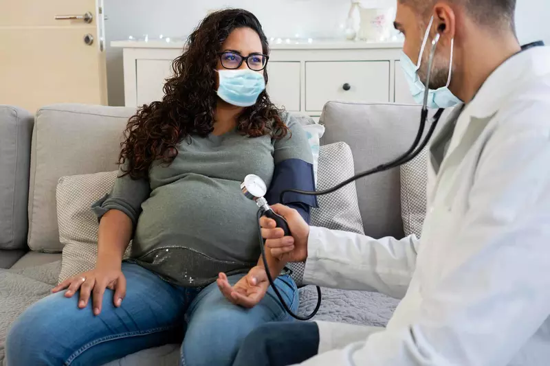 A pregnant woman has a check up while wearing a mask.