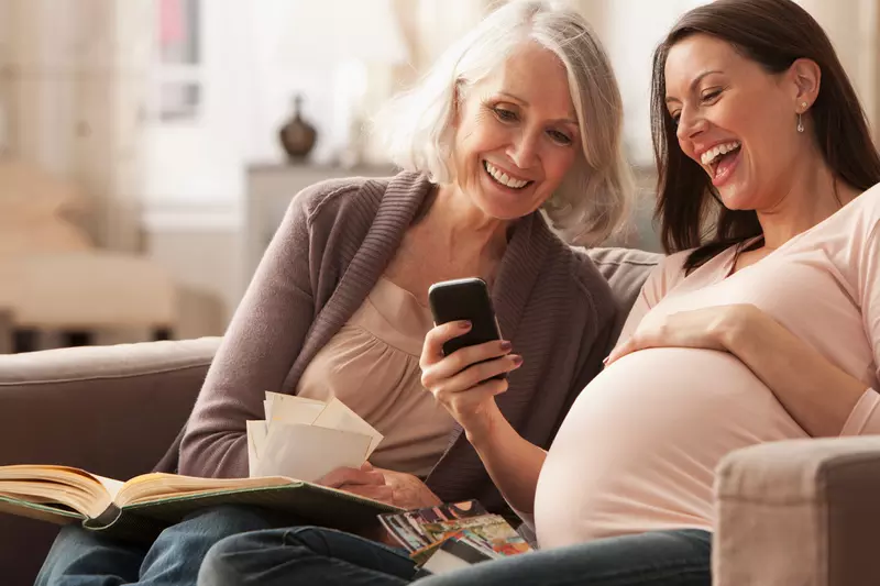 Pregnant Woman Looking at Photos on a Cell Phone with her Mom.