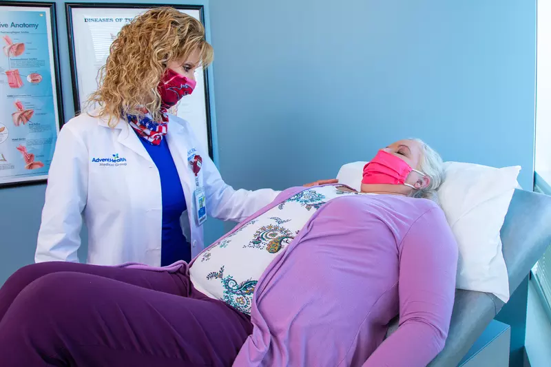 Sharona Ross examing a patient laying on an examination table while both are wearing masks.