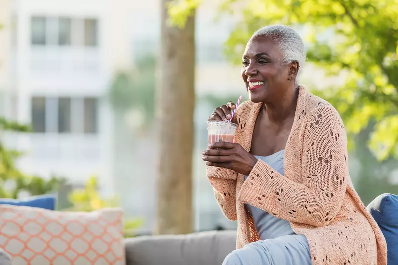 A Black Woman Enjoys a Smoothie on a Bench Outside