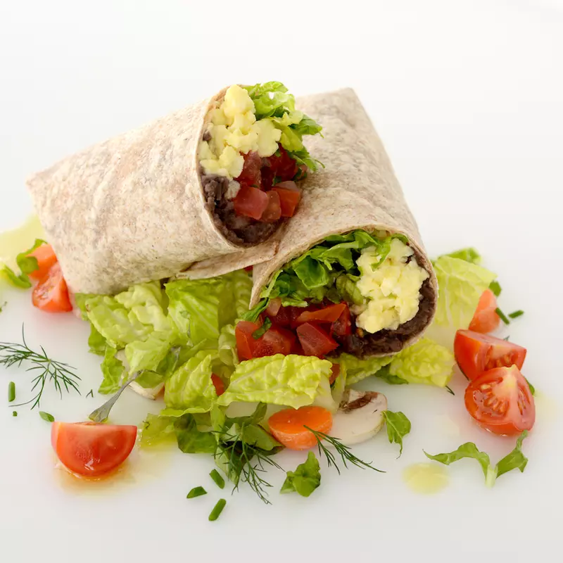 Breakfast burrito halved and stacked with tomato and green garnishes