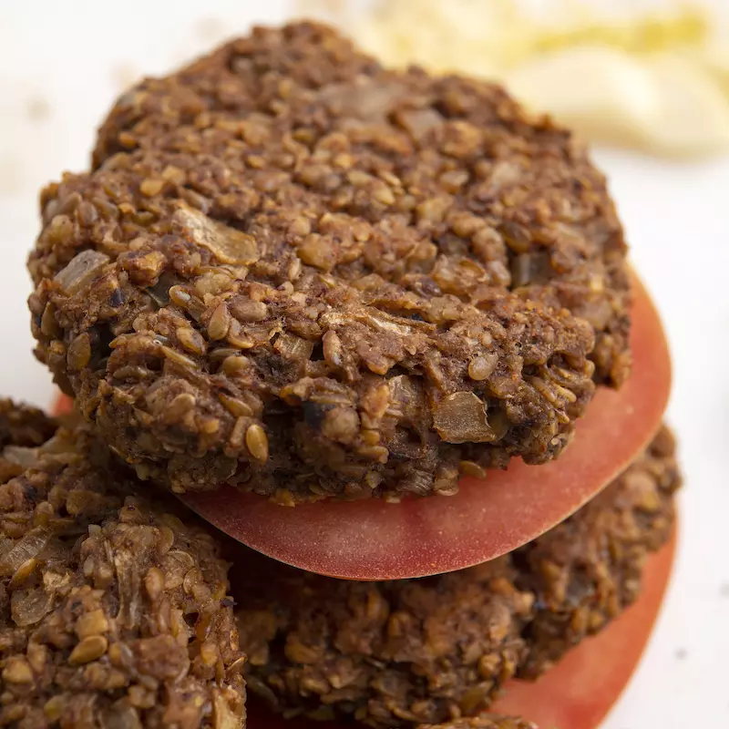 Three black bean burgers patties stacked with tomato slices