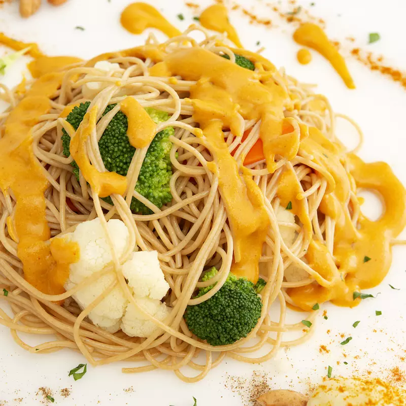 Mound of cheesy vegetable pasta on white surface