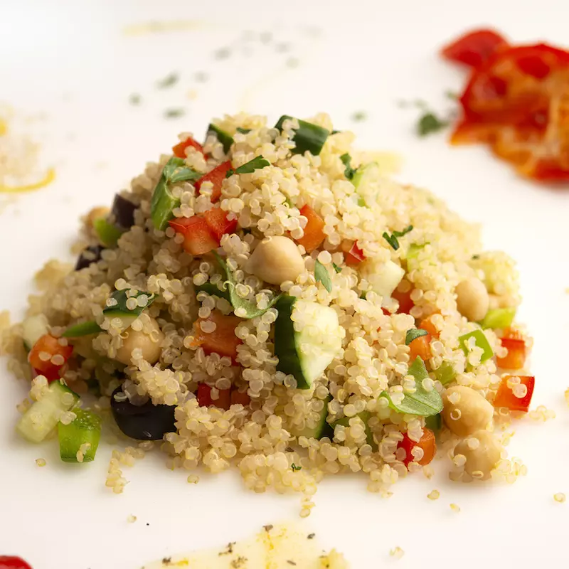 Mound of quinoa on white surface with red bell pepper garnish