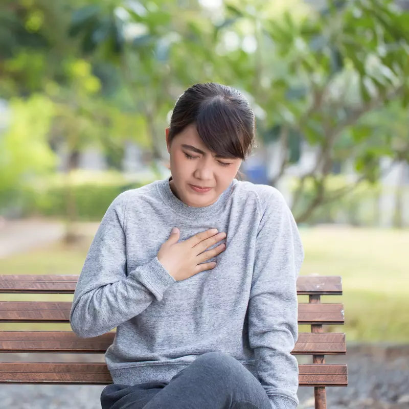 Adult woman experiencing heartburn on a bench outside