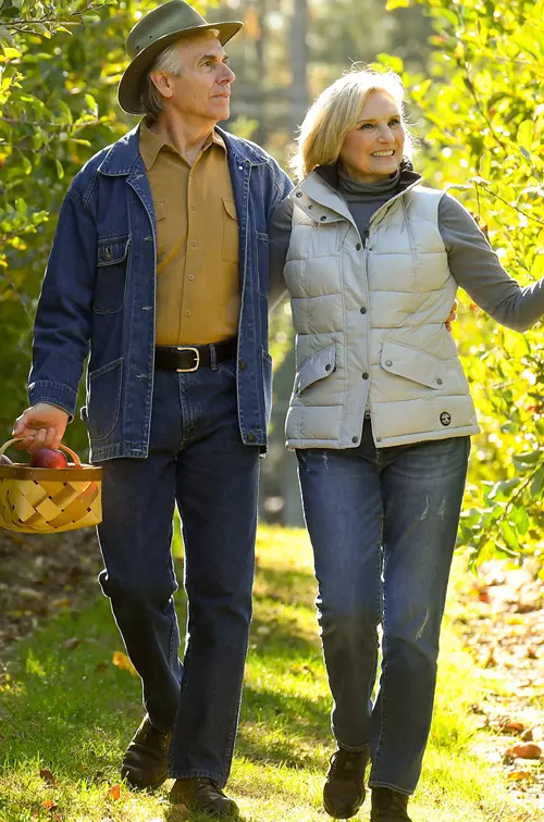 Elderly couple walking through a vineyard holding a basket.