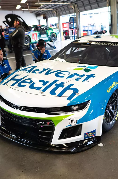 AdventHealth racing car in garage with pit crew surrounding it 