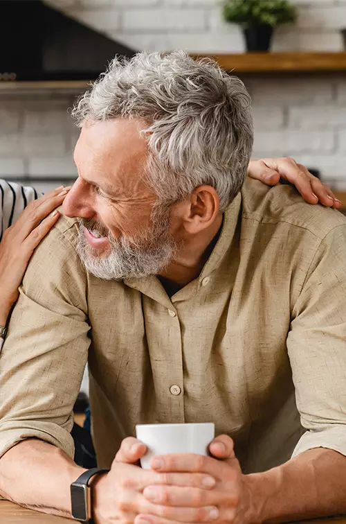 An older couple smiling at each other while in a kitchen.