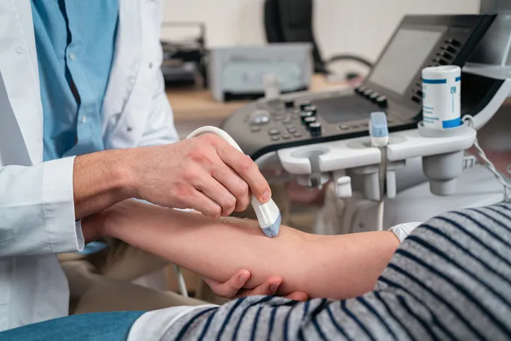At the medical clinic, unrecognizable Caucasian male doctor doing the doppler ultrasound test evaluation of arteries and veins on a senior female patient