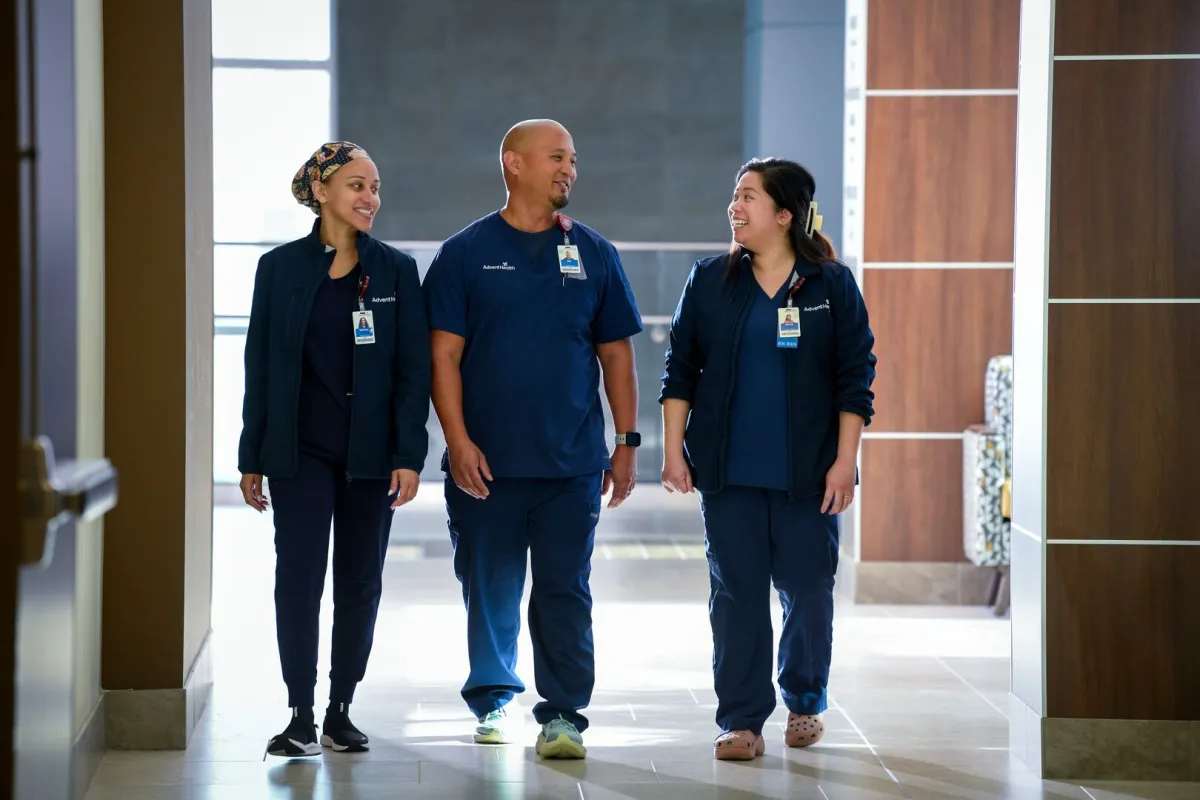 Female nurse, male nurse and another female nurse walk down a hospital hallway