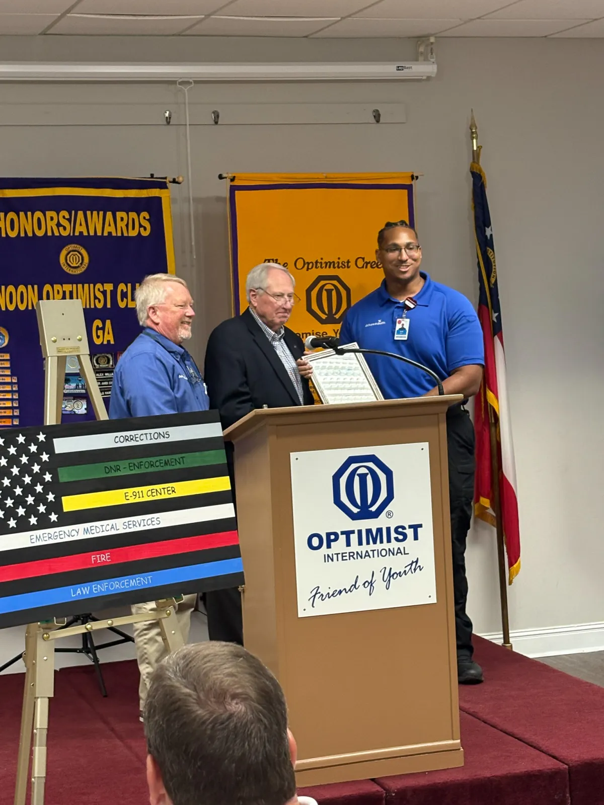 EMT Jared Firestone accepts his award from Marty Robinson and an unnamed representative of the Noon Optimist Club of Rome