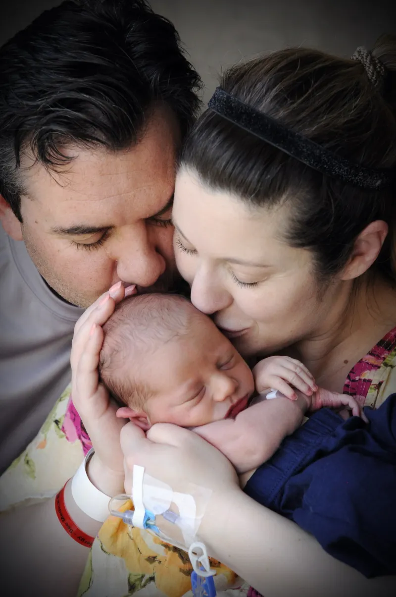 A couple holding and kissing their newborn baby.