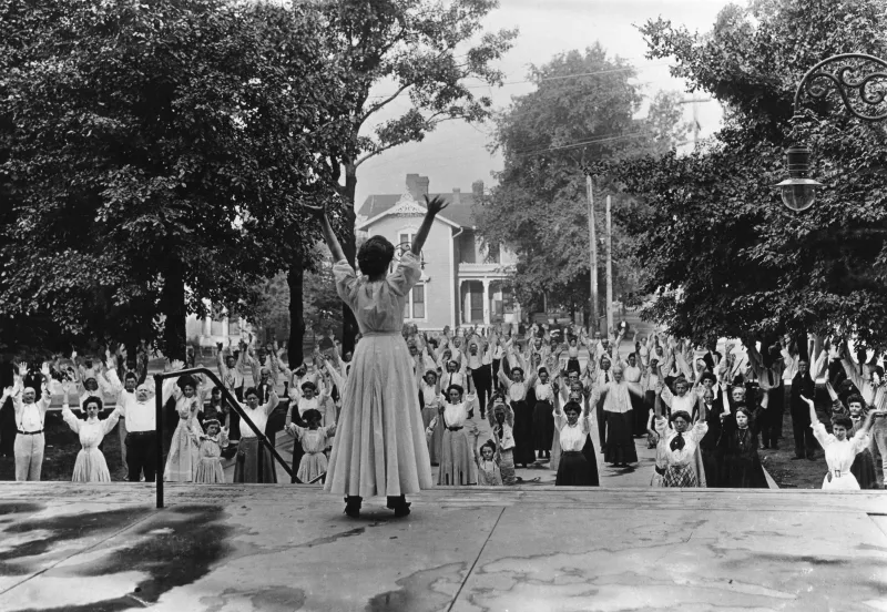 A woman leading out a group of people in breathing exercises while outdoors.